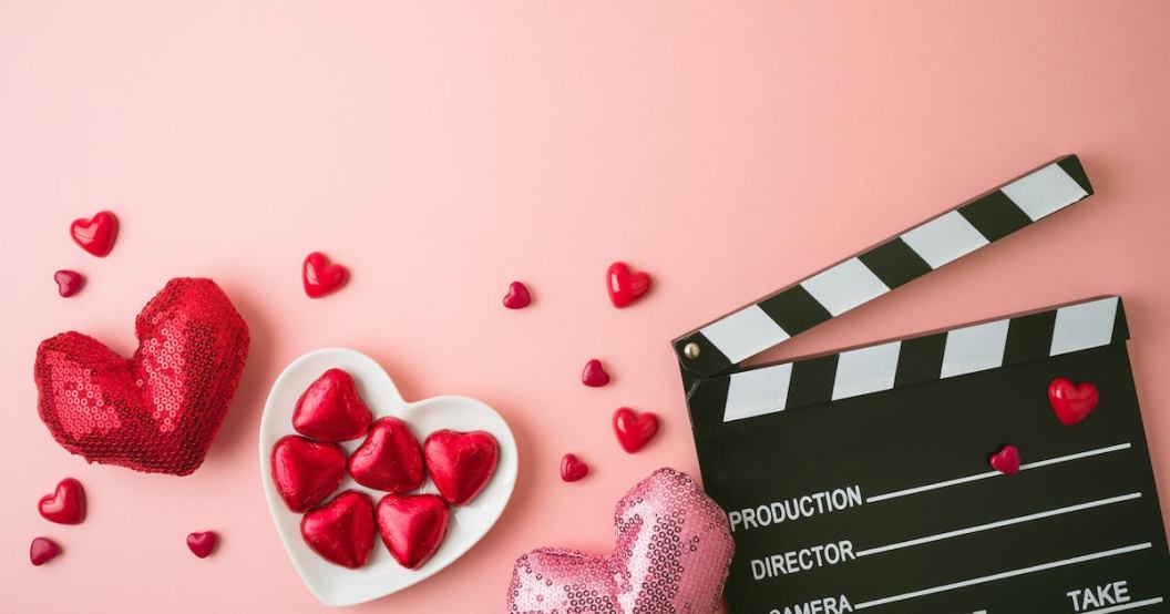 Happy Valentines day and romantic movie concept with  movie clapper board, heart shapes and chocolates on pink background. Flat lay, top view