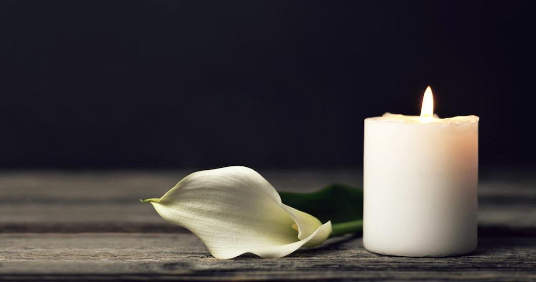 Burning candle and white calla on dark background with copy space. Sympathy card