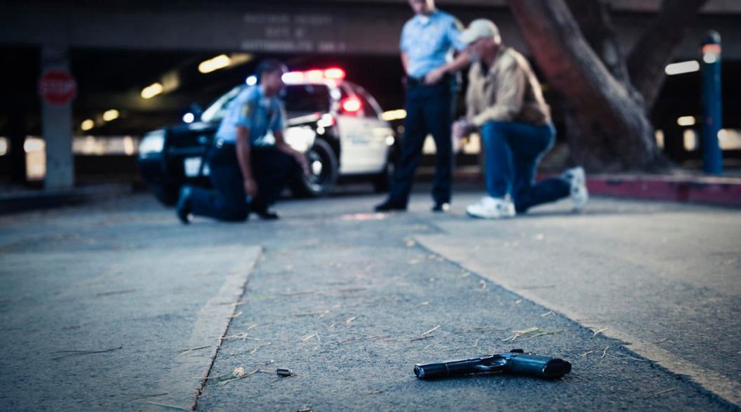 Police examining crime scene with gun on ground