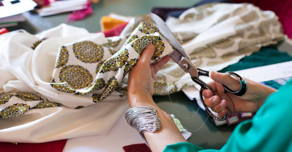 Female fashion designer at her workplace, close-up of hands cutting fabric