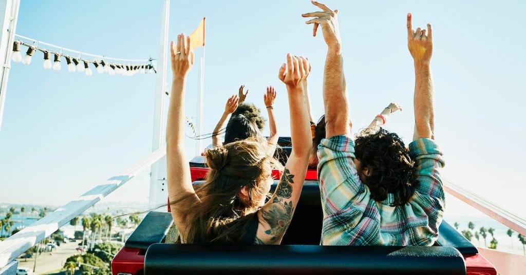 Rear view of couple with arms raised about to begin descent on roller coaster in amusement park