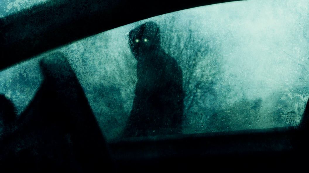 A horror concept of a spooky supernatural figure with glowing eyes. Looking into a car window on a stormy winters evening. With a blurred, textured edit.
