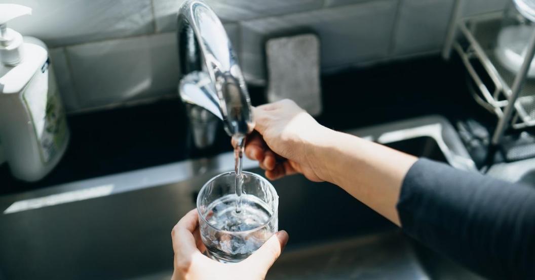 Close up of a senior woman's hand filling a glass of filtered water right from the tap in the kitchen sink at home