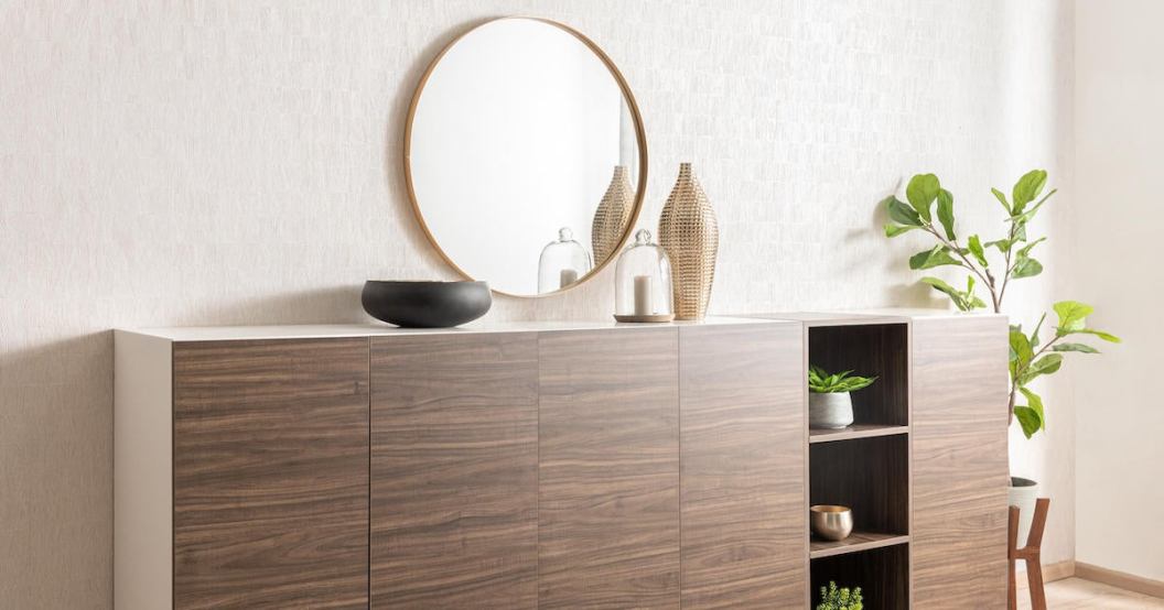 A modern wood dresser stands on a light-wood flooring, with a round mirror hanging on the wall beside it