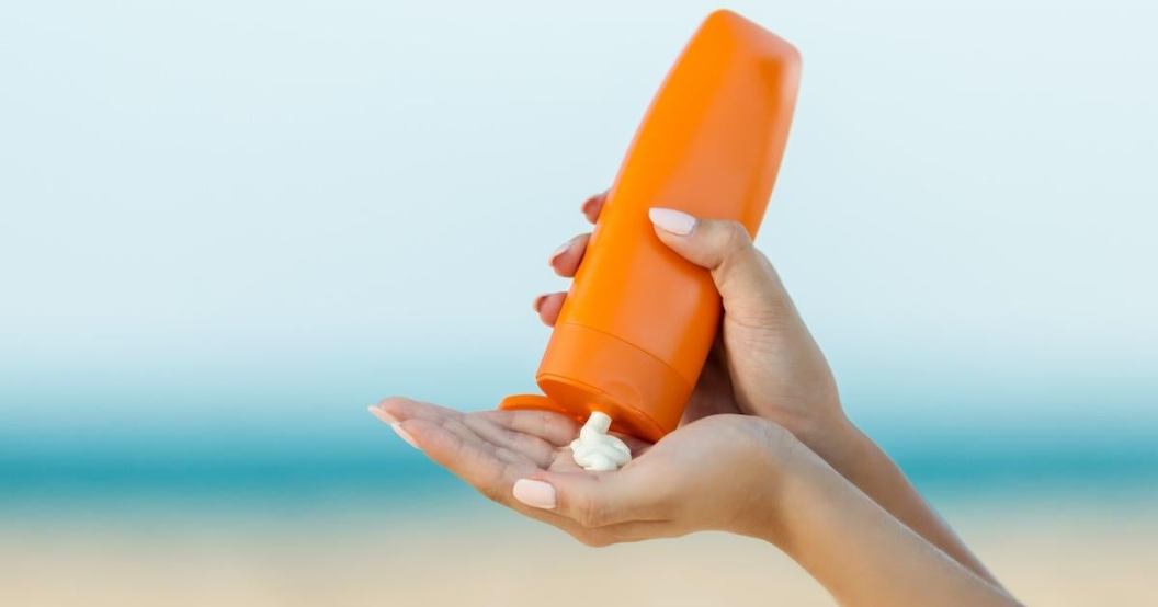 Woman hand apply sunscreen on the beach