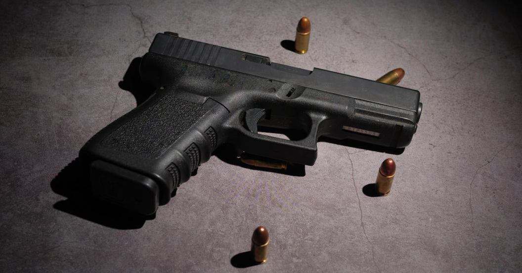 Close-up of a black metal 9mm automatic pistol with bullets all placed on a cement table with a black background.